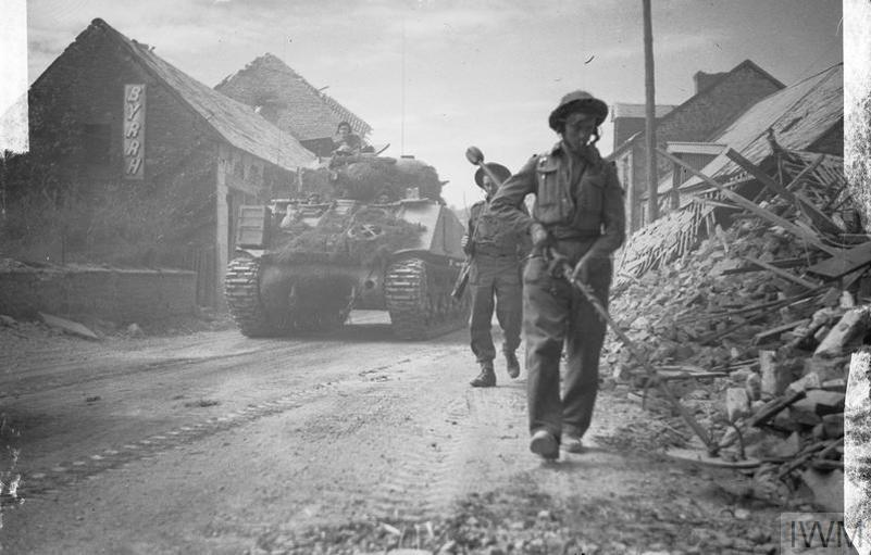 Canadian Sherman tank follows a British minesweeper down a ruined Normandy village road.