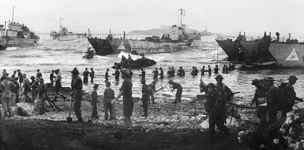 Soldiers form a line in seawater to move men and equipment off a WW2 landing craft in Sicily.