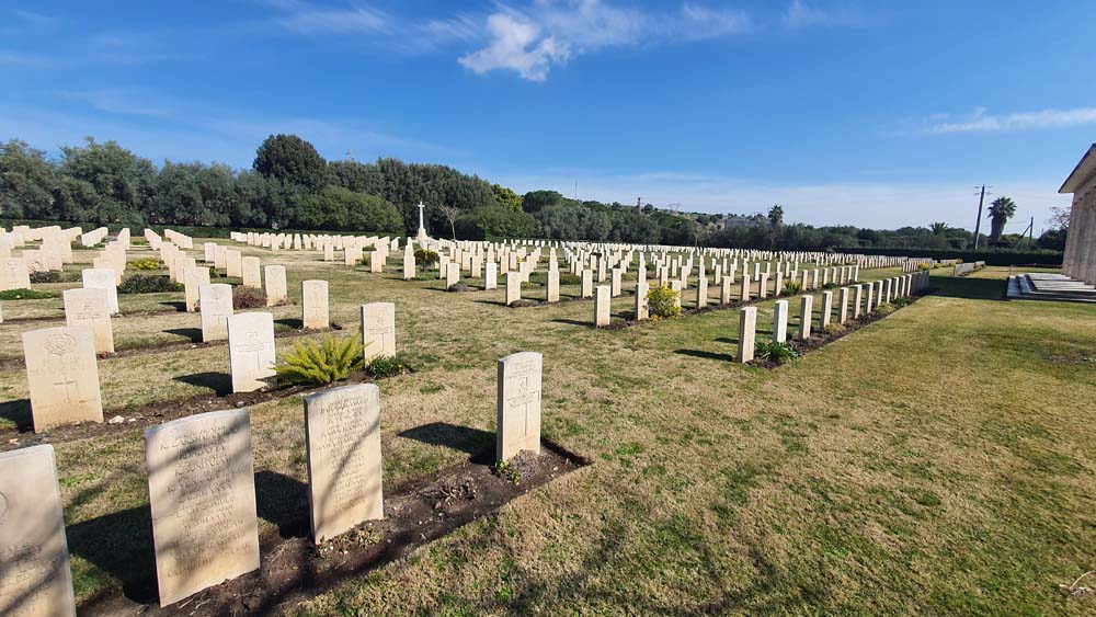 Rows of rectangular CWGC headstones at Syracuse War Cemetery. Green trees can be seen in the background under a clear blue sky.