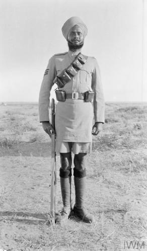 A great war era Sikh soldier standing to attention. He is wearing his fatigues with shorts and carrying a rifle.