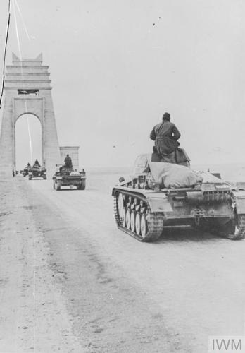 A black and white photo showing a convoy of Wehrmacht armoured vehicles passing below a high white memorial arch made in mock-Egyptian style.
