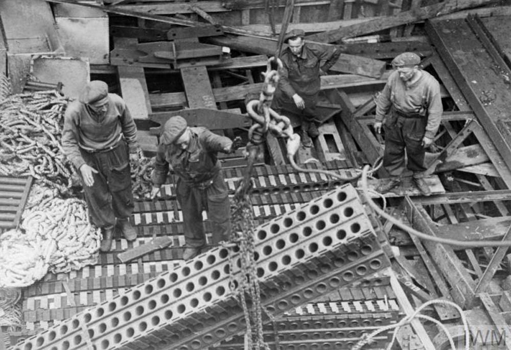 Men winch steel beams and girders off a cargo ship during World War Two.