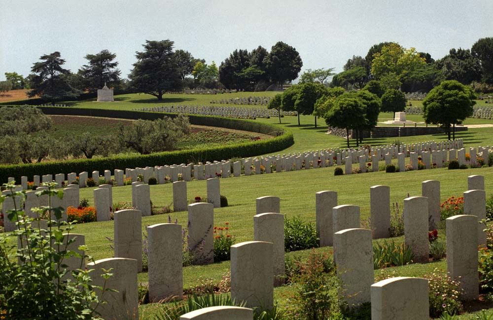 Rows of headstones at Sangro River War Cemetery. The headstones gently curve outwards, while also being positioned on a slop that leads down to a circular hedge.