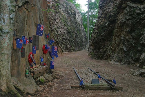 The Hellfire Pass cutting and memorial plaque showing rugged rocky cliffs and cuttings with miniature Australian flags pinned to the memorial.
