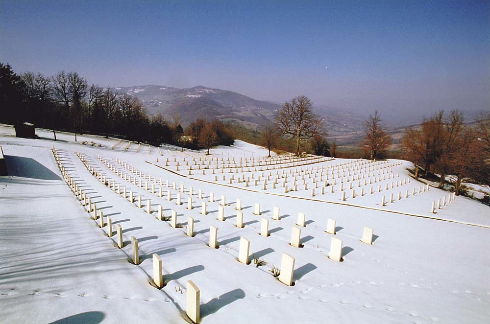 Headstones and grounds of Castiglione South African War Cemetery under a wintery blanket of snow. The rows of headstones in the cemetery are clearly visible.