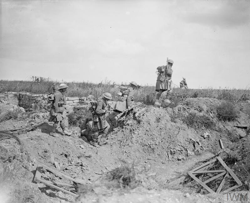 A troop of Black Watch WW1 era British soldiers going over the top of a set of trenches.