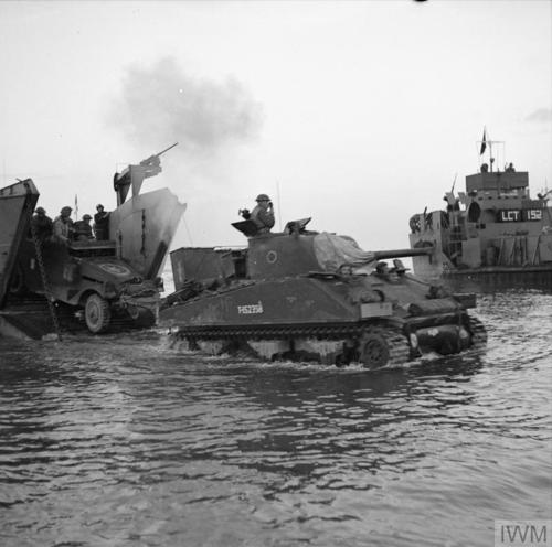 A Sherman tank drives ashore, followed by another armoured vehicle, departing from a landing craft at Anzio in 1944.