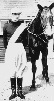 Mervyn Anythony Jones in his Jockey uniform stood next to a racehorse.