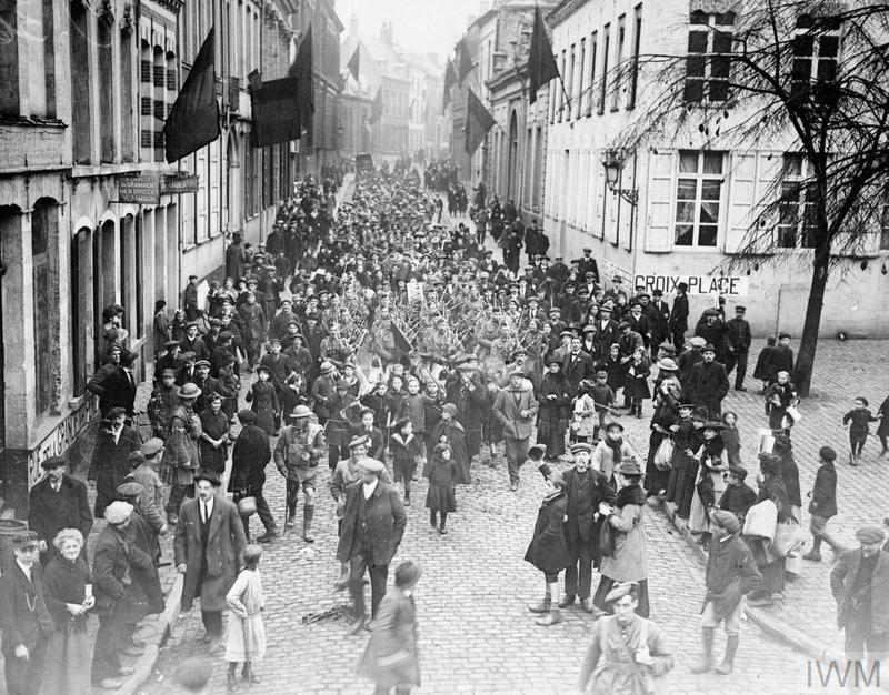 Canadian soldiers marching down a street in Mons, flanked by civilians.
