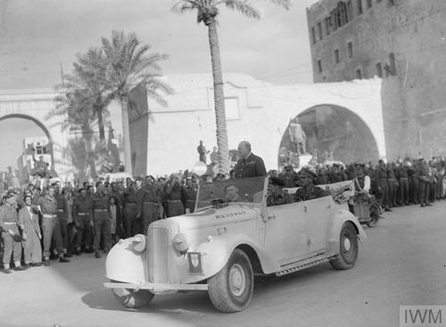 Black and white photo showing Winston Churchill standing in the back of an open topped car being received by a crowd in Tripoli.