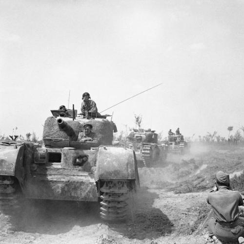 Churchill WW2 tanks advancing in a column while a squatting photographer snaps the oncoming vehicles.